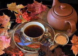 Filiżanka herbaty obok czajnika i liści klonu