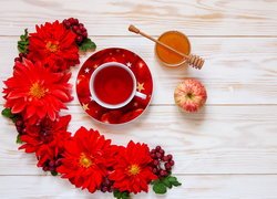 Filiżanka herbaty obok czerwonych kwiatów