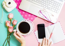 Filiżanka kawy obok róż i laptopa