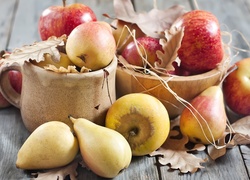 Gruszki i jabłka w naczyniach z suchymi liśćmi jako jesienna kompozycja