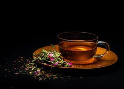 Herbata w filiżance z płatkami kwiatów na spodku