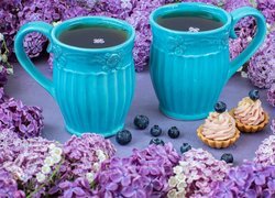 Herbata w kubkach obok babeczek i kwiatów bzu