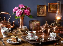 Hortensje i lampa naftowa obok zestawu do herbaty i ciasta