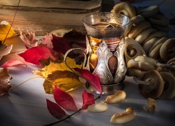 Jesienna kompozycja z liści obok szklanki z herbatą i obwarzanków