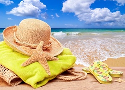 Kapelusz na plażowym ręczniku obok klapek na morskiej plaży