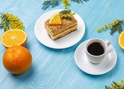 Kawałek ciasta na talerzyku obok pomarańczy i kawy