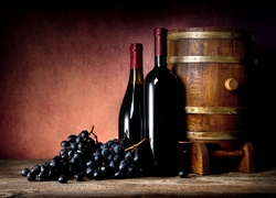 Kiście winogron położone obok butelek i beczki z winem