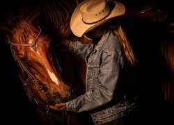 Kobieta w kapeluszu obok konia na ciemnym tle