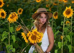 Kobieta w kapeluszu z kwiatami na słonecznikowym polu