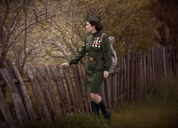 Kobieta w mundurze z odznaczeniami przy drewnianym płocie