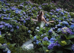 Kobieta w ślubnej sukni pośród kwiatów hortensji