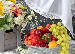 Kompozycja z bukietu kwiatów w skrzynce i owoców na szklanej paterze