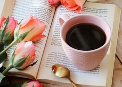 Kubek kawy na otwartej książce obok róż