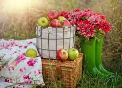 Kwiaty w kaloszach obok kosza piknikowego i jabłek w torbie