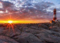 Latarnia morska na skałach w promieniach zachodzącego słońca