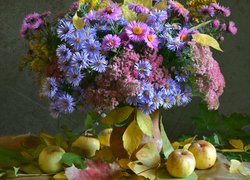 Liście i jabłka wokół wazonu z jesiennym bukietem