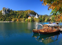 Łódki na brzegu jeziora Bled i widok na zamek i kościół w oddali