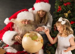Mikołaj i kobieta z dziewczynką obok globusu i choinki