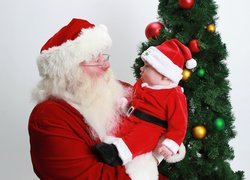 Mikołaj z dzieckiem w stroju mikołaja na rękach obok choinki