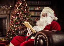 Mikołaj z książką na fotelu obok choinki