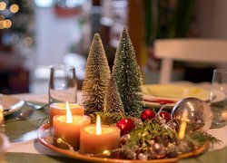 Miniaturowe choinki i świece w świątecznym stroiku
