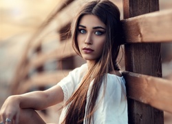 Niebieskooka dziewczyna z długimi włosami oparta o drewniane ogrodzenie