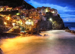 Oświetlone domy na skałach nad morzem we włoskiej miejscowości Manarola
