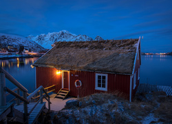 Oświetlony dom nad jeziorem w norweskiej wiosce Reine nocą
