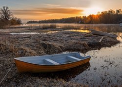 Oszronione łódki na brzegu jeziora o zachodzie słońca