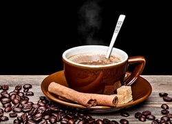 Parująca kawa w filiżance i ziarna rozsypane na blacie