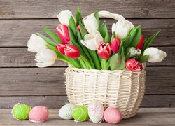 Pisanki obok białych i czerwonych tulipanów w białym koszyku
