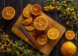 Pomarańcze na desce wśród gałązek z żółtymi kwiatkami