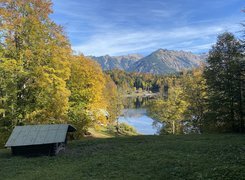 Pożółkłe drzewa i domy nad jeziorem na tle gór