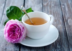 Róża położona na talerzyku obok filiżanki z herbatą