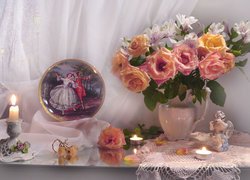 Róże i alstremerie w wazonie obok świec i figurki aniołka