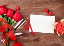 Róże i kieliszki obok prezentu i kartki