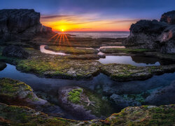Rozświetlone blaskiem zachodzącego słońca omszałe skały nad morzem