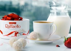 Słodycze Raffaello obok filiżanki z herbatą i dzbanka z mlekiem