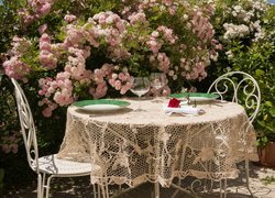 Stół i krzesła pod krzewami róż w ogrodzie