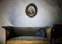 Torebka położona na starej sofie i portret wiszący na popękanej ścianie