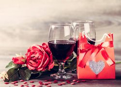 Torebka z prezentem obok kieliszków z winem i róży