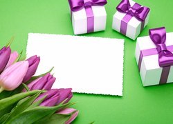 Trzy prezenty obok białej kartki i fioletowych tulipanów