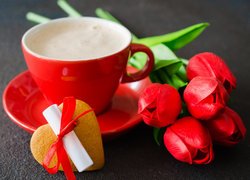 Tulipany obok filiżanki kawy i ciasteczkiem z liścikiem