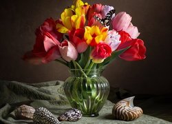 Tulipany w szklanym wazonie pośród muszelek