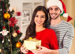 Uśmiechnięta kobieta i mężczyzna z prezentem obok choinki