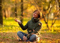 Uśmiechnięta kobieta patrząca na spadające liście