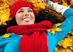 Uśmiechnięta kobieta w czapce i szaliku leżąca na liściach