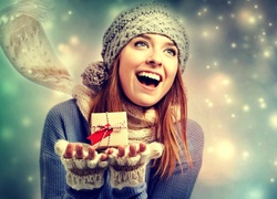 Uśmiechnięta kobieta z prezentem na dłoniach w zimowo-świątecznym klimacie