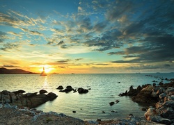 Widok z brzegu morza na żaglówkę w zachodzącym słońcu