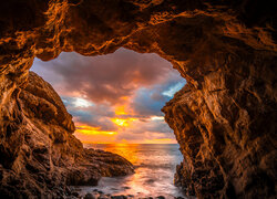 Widok z rozświetlonej jaskini na zachód słońca nad morzem